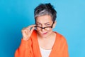 Photo portrait of lovely senior lady touch specs skeptical look dressed stylish orange garment isolated on blue color Royalty Free Stock Photo