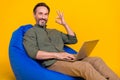 Photo portrait man sitting in chair with laptop showing okay sign isolated bright yellow color background Royalty Free Stock Photo