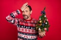 Photo portrait man with small xmas tree upset forgot touching forehead isolated vibrant red color background