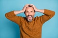 Photo portrait of middle-aged bearded man amazed shocked keeping head with hands shouting isolated on vibrant blue color