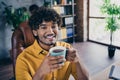 Photo portrait of nice young male wear yellow shirt enjoy morning coffee comfort work sit table living room interior Royalty Free Stock Photo