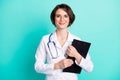 Photo portrait of nurse smiling embracing clipboard wearing white uniform isolated vivid teal color background