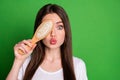 Photo portrait of pouting girl covering one eye with hairbrush isolated on vivid green colored background Royalty Free Stock Photo