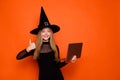 Photo portrait of pretty blonde teenager girl netbook showing thumb up dressed black halloween outfit isolated on orange Royalty Free Stock Photo