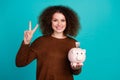 Photo portrait of pretty young girl piggy money account show v-sign dressed stylish brown outfit isolated on aquamarine