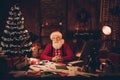 Photo portrait santa claus sitting at table in room near decorated xmas tree wearing glasses headwear Royalty Free Stock Photo