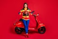 Photo portrait of screaming girl holding helmet in two hnads sitting on scooter isolated on vivid red colored background