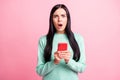 Photo portrait of shocked upset girl holding phone with two hands on pastel pink colored background