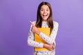 Photo portrait of surprised female pupil keeping yellow copybook pointing at blank space isolated on vibrant violet Royalty Free Stock Photo