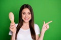 Photo portrait of woman pointing finger to side holding hairbrush in hand isolated on vivid green colored background