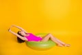 Photo portrait of woman stretching on inflatable green circle wearing pink swim wear  on vivid yellow colored Royalty Free Stock Photo