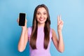 Photo portrait of young girl demonstrating mobile phone touchscreen copyspace showing v-sign isolated on vivid blue Royalty Free Stock Photo