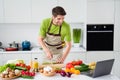 Photo portrait young man in apron cooking vegetables salad slicing cucumber watching video on laptop Royalty Free Stock Photo