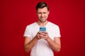 Photo portrait of young man unhappy stressed reading fake news cellphone biting lip isolated vibrant red color