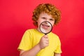 Photo of positive candid ginger small boy magnifying glass show teeth wear yellow t-shirt isolated red color background Royalty Free Stock Photo