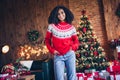 Photo of positive charming girl put hands pockets posing new year illumination evergreen tree gifts living room flat