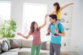 Photo of positive cheerful three people mommy daddy carry shoulders little kid girl hold hand in house indoors