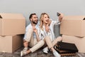Photo of positive couple seating near cardboard boxes and taking selfie photo on cellphone