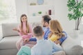 Photo of positive cute kid girl sit couch talk news with mommy daddy brother in house indoors