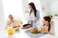 Photo of positive family little sweet girl cheerful satisfied parents eat delicious food prepare frying pan modern