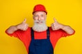 Photo of positive funky age man workwear overall red hard hat showing two thumbs up isolated yellow color background Royalty Free Stock Photo