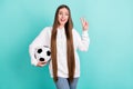 Photo of positive happy young woman hold hand football make v-sign isolated on pastel teal color background