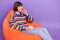 Photo of positive lady sit beanbag eat popcorn enjoy cinema wear striped pullover isolated violet color background