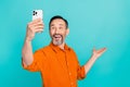 Photo of positive man with gray beard making selfie photo on smartphone arm presenting empty space isolated on teal Royalty Free Stock Photo