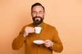 Photo of positive man hold cup drink closed eyes wear eyeglasses brown cardigan isolated beige color background