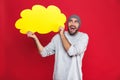 Photo of positive man smiling and holding blank thought bubble isolated over red background Royalty Free Stock Photo