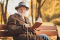 Photo of positive old man enjoy reading knowledge book story in fall nature town center park sit bench hold walk stick