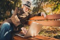 Photo of positive old man rest relax autumn colorful holiday forest city center park sit bench use laptop chat son