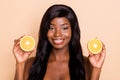 Photo of positive pretty lady presenting two orange slices look camera beaming smile isolated beige background Royalty Free Stock Photo