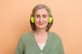 Photo of positive senior grandmother listen wireless headphones pop jazz music soundtrack relax time isolated on beige