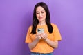 Photo of positive woman with straight hairdo dressed orange t-shirt read message on smartphone isolated on purple color