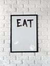 Photo of poster with text Eat in a black frame on a white brick wall. Empty space for text. Royalty Free Stock Photo