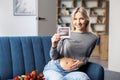 Photo of a pregnant woman at home sitting on couch near beautiful bouquet, holding in her hand baby ultrasound scan print Royalty Free Stock Photo