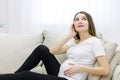 Photo of pregnant woman on white sofa touching her stomach and face. Royalty Free Stock Photo