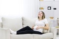 Photo of pregnant woman on white sofa touching her stomach. Royalty Free Stock Photo