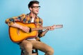 Photo of pretty adorable guy dressed plaid shirt spectacles smiling siting chair playing guitar empty space isolated Royalty Free Stock Photo