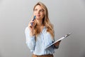 Photo of pretty blond secretary woman with long curly hair thinking and holding clipboard while working in office Royalty Free Stock Photo