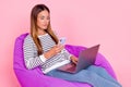 Photo of pretty busy mature lady wear striped sweater smiling sitting beanbag working modern gadgets pink color