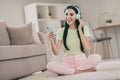 Photo of pretty carefree girl sit carpet crossed legs open mouth hold telephone wear earphones green t-shirt pink Royalty Free Stock Photo