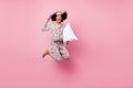 Photo of pretty charming curly dark skin woman dotted nightwear rising fist holding white pillow jumping high isolated