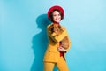 Photo of pretty charming young lady wear yellow blazer red cap smiling holding small friend isolated blue color