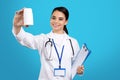 Photo of pretty charming young woman doctor holding bottle of pills and clipboard over blue background. Royalty Free Stock Photo