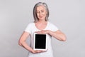 Photo of pretty cheerful manager elder lady show look tablet wear white t-shirt isolated on grey color background