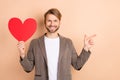 Photo of pretty classy gentleman dressed blazer holding big red heart pointing finger empty space isolated beige color Royalty Free Stock Photo
