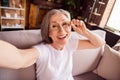 Photo of pretty cute lady pensioner wear white t-shirt sitting sofa smiling tacking selfie indoors house flat