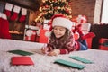 Photo of pretty cute school girl wear print pullover headwear smiling lying floor writing letter indoors house home room Royalty Free Stock Photo